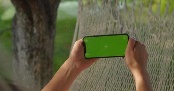 Młode kobiety spoczywa w hamaku patrząc na boczny telefon z zielonym ekranem — Wideo stockowe
