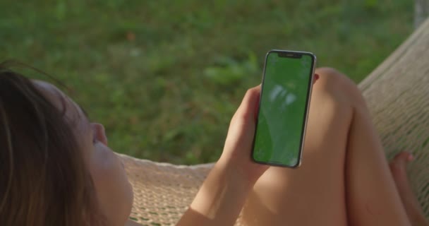 Młode kobiety spoczywa w hamaku patrząc na pionowy telefon z zielonym ekranem — Wideo stockowe