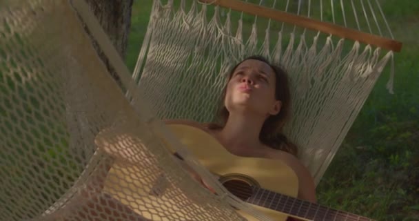 Brunette girl has rest in hammock and plays guitar singing — Wideo stockowe