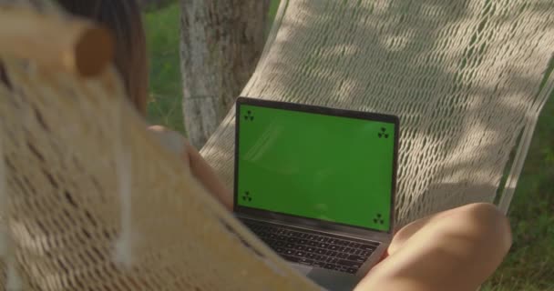 Teen girl swings in hammock working on laptop green screen — Wideo stockowe