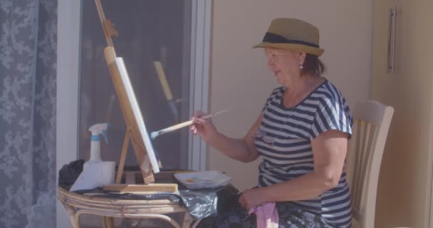 Uśmiechnięta emerytka w pasiastej koszulce rysuje malarstwo — Wideo stockowe