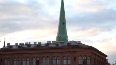 Letonya 'nın Riga kasabasında, Avrupa' nın tarihi mimarisi. Riga Bourse Sanat Müzesi 'nin ön cephesi ve çatısına bir manzara ve arkalarında mavi bulutlu arka planda bir kilise kulesi..