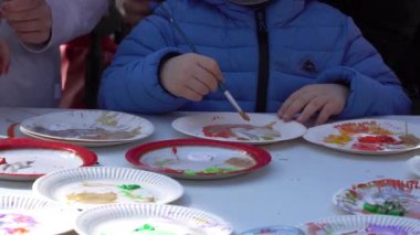 Renklerle resim yapan çocuklar. Paskalya bayramında çocuklu aileler için açık hava renk yaratıcı atölyesi. Tabaklar boyalarla dolu bir masada..