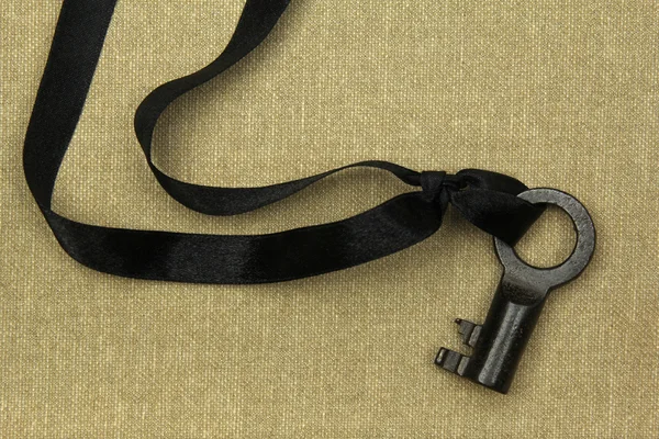 Old key with black ribbon on natural linen — Stock Photo, Image