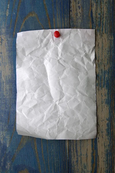 Kırmızı itme ile beyaz buruşuk kağıt mavi ahşap arka plan üzerinde pin — Stok fotoğraf