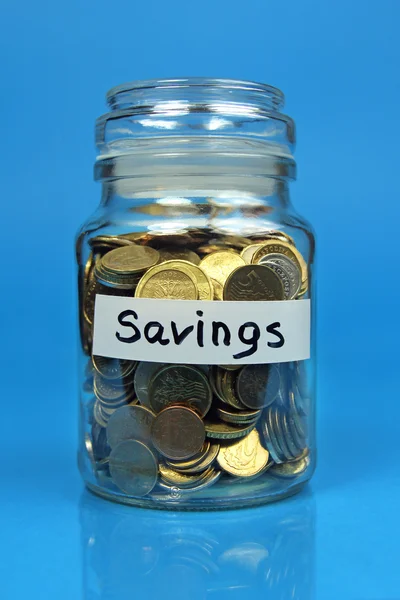 Coins in jar with savings label on blue background — Stock Photo, Image