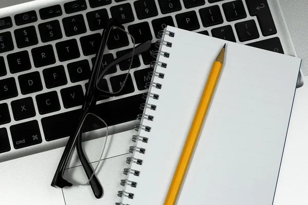 Zbliżenie okulary, notatnik i ołówek na laptopie srebrny — Zdjęcie stockowe