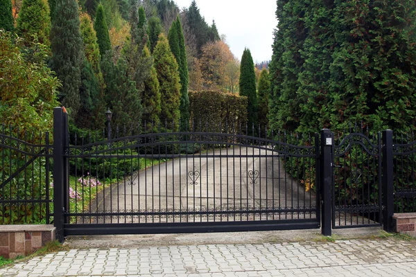 Czarny kute bramy do Właściwość z ogrodem w tle — Zdjęcie stockowe