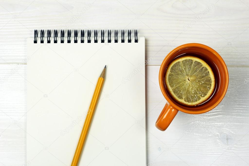 Blank notebook with pen and cup of tea on white wooden surface