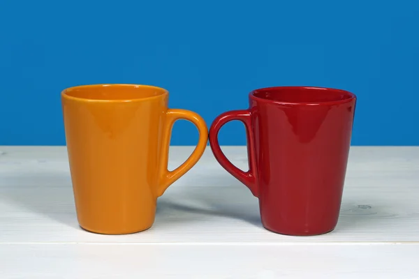Dos tazas de café de colores sobre mesa de madera blanca sobre fondo azul —  Fotos de Stock