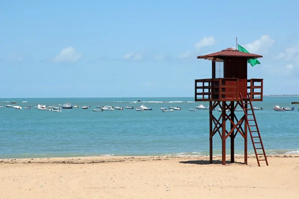 Beach with lifeguard post and fishing boats in the background — Stock Photo, Image