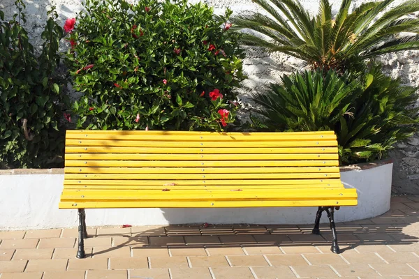 Yellow wooden bench with palms in the background — Stock Photo, Image