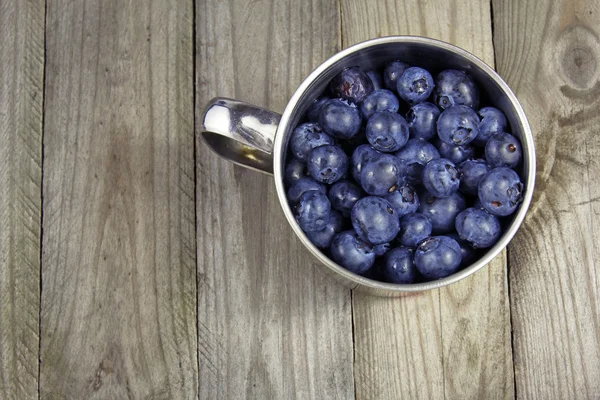 Blueberries in metal cup on wooden background or texture — Stock Photo, Image