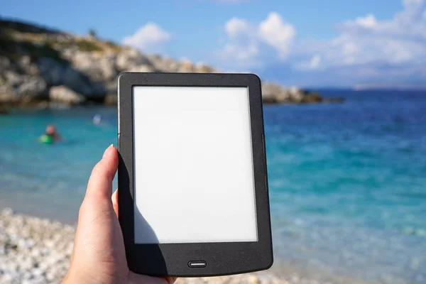 在海滩上手持电子书阅读器 在暑假期间看书 — 图库照片