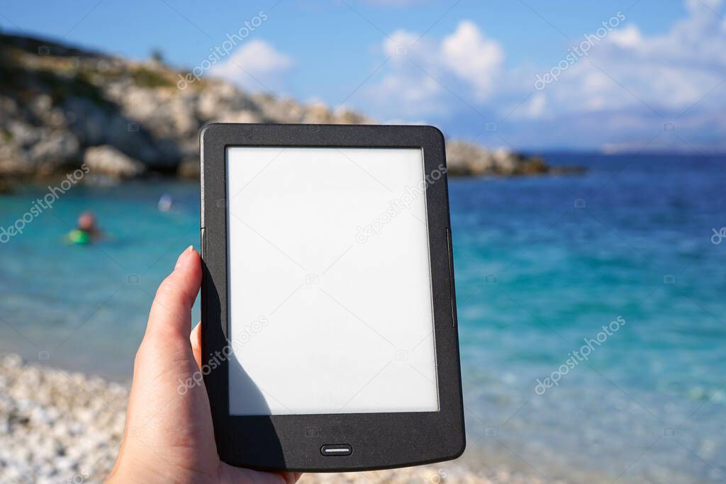 hand holding e-book reader on the beach, reading during summer vacation