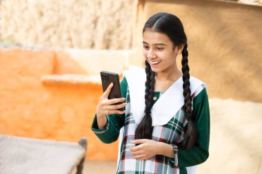 Mutlu Kırsal Kır Kızı akıllı telefondan video çağrısı yapıyor, neşeli örgü ören kadın dijital android cep telefonu ya da cep telefonu kullanıyor, konuşuyor, yetenekli Hindistan.
