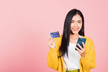 Mutlu bir Asyalı portresi güzel tatlı bir genç kadın gülümseyen cep telefonu ve plastik banka kartı, stüdyo resmi pembe arka planda, akıllı telefon kullanan bir kadın online alışveriş yapıyor.