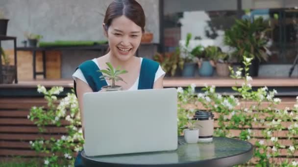 アジアの美しいライフスタイルの若い女性は ノートパソコンのコンピュータによる小さな木やサボテンをオンラインで販売話ソーシャルメディアライブストリーミング 温室近くのビジネスオンライン電子商取引距離 中小企業 — ストック動画