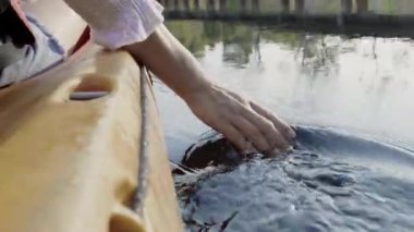 Arka tarafta genç yetişkin bir kadın göl kenarındaki bir kano teknesinde el ele tutuşuyor. Yaz günü şeffaf bir suya dokunuyor. Macera seyahati keyfi konsepti, yaşam tarzı spor tatili.