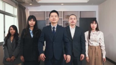 Başarılı bir grup iş adamı ofiste kollarını kavuşturup gülümsüyor, takım elbiseli iş adamları kollarını göğsünün üstüne koyup kameraya bakıyorlar.