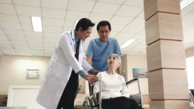 Doktor, tekerlekli sandalyedeki yaşlı kadın hasta ve hemşire adamla konuşuyor. Hastane koridorunda ameliyattan önce ileri doğru ilerliyorlar.
