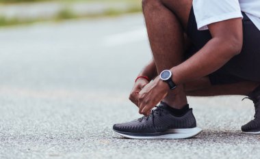 Kapatın Asyalı spor koşucusu siyah adam kol saati takıyor ayakkabı bağcığı deniyor koşuya hazırlanıyor ve sağlık parkında koşuyor, sağlıklı egzersiz konsepti.