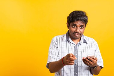 Yakın plan Asyalı mutlu portre genç zenci bir cep telefonu tutuyor ve kamerayı işaret ediyor. Stüdyo sarı arka planda izole edilmiş.