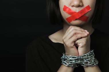 Asyalı bir kadın, ağzı kırmızı bantla kapatmış ve elleri siyah arka planda bağlanmış. Konuşma özgürlüğü sansürü ve konuşmayı durdurmak, Uluslararası İnsan Hakları Günü