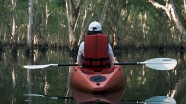 Gölde kano süren genç bir kadın yaz günü akıllı telefonuyla fotoğraf çekiyor. Macera seyahati keyfi konsepti, yaşam tarzı spor tatili.