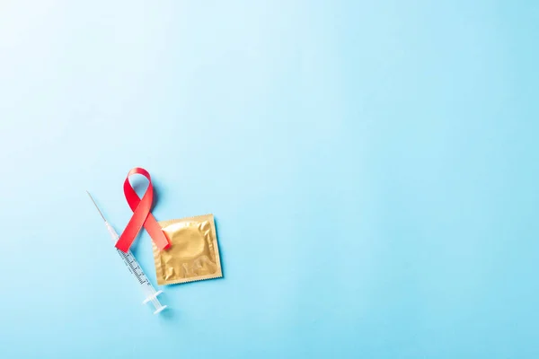 红弓带标志着艾滋病毒 对艾滋病的认识 带阴影的避孕套和注射器 隔离在蓝色背景下的演播室镜头 医疗保健医学的性概念 世界艾滋病日 — 图库照片