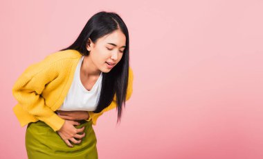 Portrait of Asian beautiful young woman has stomachache, female abdominal pain suffering from stomach ache, studio shot isolated on pink background, Health and medical gastritis concept