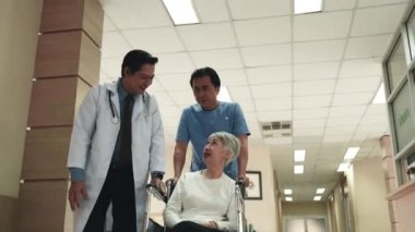 Doktor, tekerlekli sandalyedeki yaşlı kadın hasta ve hemşire adamla konuşuyor. Hastane koridorunda ameliyattan önce ileri doğru ilerliyorlar.