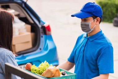 Asyalı genç teslimatçı yüz maskesi takıyor markete hızlı servis yapıyor kadın müşterilere plastik sepette taze sebze veriyor pandemik koronavirüsten sonra evlerinin kapısına geliyor.