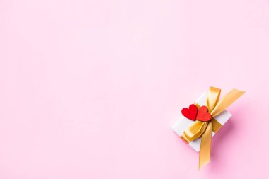 Sevgililer Günü geçmişi konsepti. Altın kurdeleli beyaz hediye kutusu ve ahşap kırmızı kalpler kompozisyon tebrik kartı. Pembe arka planda izole edilmiş ve fotokopi alanı olan mutlu aşk için. Yukarıdan görüntüle