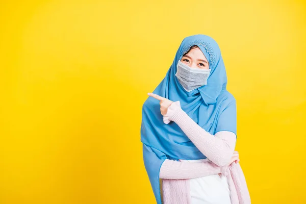 アジアのイスラム教徒のアラブ人 幸せな美しい若い女性の肖像画宗教的な服のベールヒジャーブと顔のマスク保護彼女は指の側の距離のスペースを指すコロナウイルスを防ぐために 黄色の背景に隔離 — ストック写真