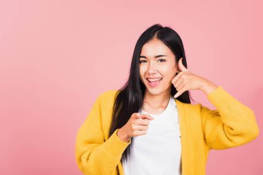 Asyalı güzel, gülümseyen, telefonla el hareketi yapan ve kamerayı işaret eden genç bir kadının portresi. Beni geri ararken stüdyo görüntüsü izole edilmiş pembe arka plan.