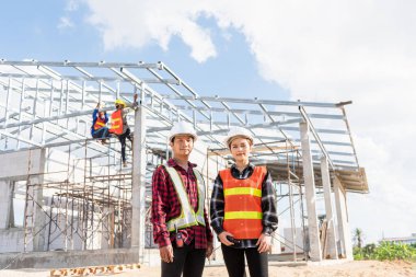 Mimar ve müvekkil ev inşaatında duruyor. Asyalı mühendis ustabaşı işçi ve kadın inşaat üzerine poz veriyor.