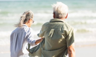 Mutlu Asyalı üst düzey erkek ve kadın çift el ele tutuşarak kumsala yürüyorlar açık mavi gökyüzü ile, romantik yaşlılar yaz tatilinin tadını çıkarıyorlar, emekliler konseptinde hayat sigortası planlıyorlar.