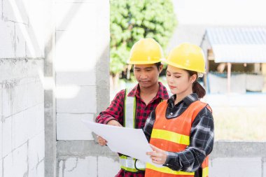 Mimar ve müvekkil, inşaat alanındaki binanın planıyla planı tartışıyor. Asyalı mühendis ustabaşı erkek ve kadın, projeyi kontrol etmek için konuşma ve çizim kağıtları üzerinde çalışıyorlar.