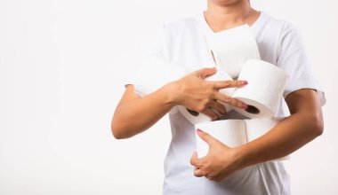 Koronavirüs karantinasında ev paniği için tuvalet kağıdı stoklayan Asyalı genç bir kadın. Göğüs kafesinde bir sürü tuvalet kağıdı tutan kadın, beyaz arka planda izole edilmiş stüdyo.