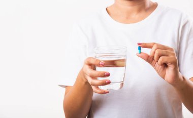 Yakın plan genç Asyalı kadın elinde haplarla hazır bir bardak suyla ilaç alıyor, beyaz arka plan, sağlık ve tıbbi eczane konseptine izole edilmiş stüdyo fotoğrafları çekiyor.