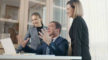 Kazananların başarı projesini kutluyoruz. Üç mutlu iş adamı birlikte iyi haberler aldıkları için heyecanlı. Başarılı projeyi masa başındaki dizüstü bilgisayarla kutluyorlar.