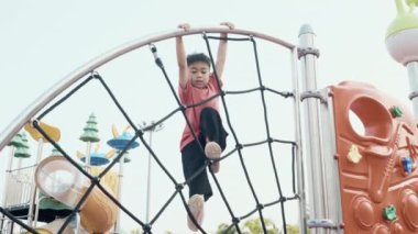 Asyalı bir çocuk gülerek oyun parkına tırmanır, anaokulunda mutlu bir şekilde eğlenir ve yaz aylarında oyun parkındaki ekipmanların üzerinde tırmanır.