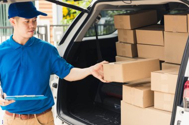 Üniformalı Asyalı genç kurye evrakları pano kontrol listesi posta kutularını müşteriye servis sevkiyatı için bir arabanın yanında tutuyor, çevrimiçi alışveriş hizmeti kavramları