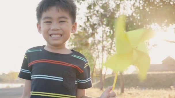 바람개비를 가지고 아시아인 정원에서 여름날작은 바람개비나 장난감을 밀밭에서 미소짓고 — 비디오