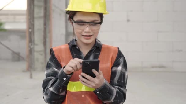 Asijský architekt inženýr pracovník žena v ochranné přilbě a uniformě pomocí chytrého telefonu mobilní aplikace s týmem na plánování a developerské projekty při práci na staveništi domu