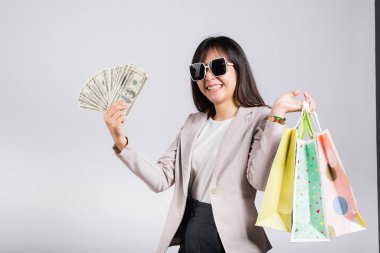 Gözlüklü, kendine güvenen, alışveriş torbaları tutan, elinde para banknotları olan, mutlu Asyalı genç bayan stüdyosu beyaz arka planda izole edilmiş mutlu, mutlu, genç bir bayan.