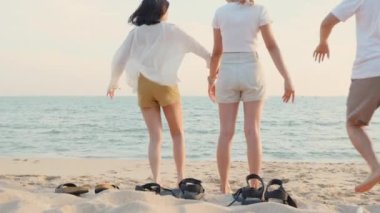 Mutlu arkadaşlar el ele tutuşup hayatın tadını çıkarıyorlar kumsalda birlikte özgürlüğün tadını çıkarıyorlar gün batımında tatil tatilinde genç Asyalı kadın ve erkek yaz seyahatinde, insanların yaşam tarzı