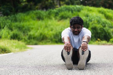Kapatın Asyalı genç sporcu spor koşucusu siyah adam kol saati takıyor ayak parmaklarını uzatıyor bacaklarını ve dizlerini esnetiyor açık hava parkına koşmadan önce spor konseptinden önce sağlıklı egzersiz.