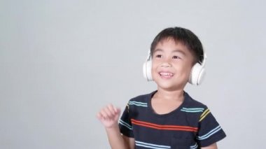5-6 yaşlarında şirin bir çocuk. Beyaz arka planda izole edilmiş kablosuz kulaklıklarla müzik dinliyor. Mutlu Asyalı çocuklar gülerek ses ve dans dinliyor.